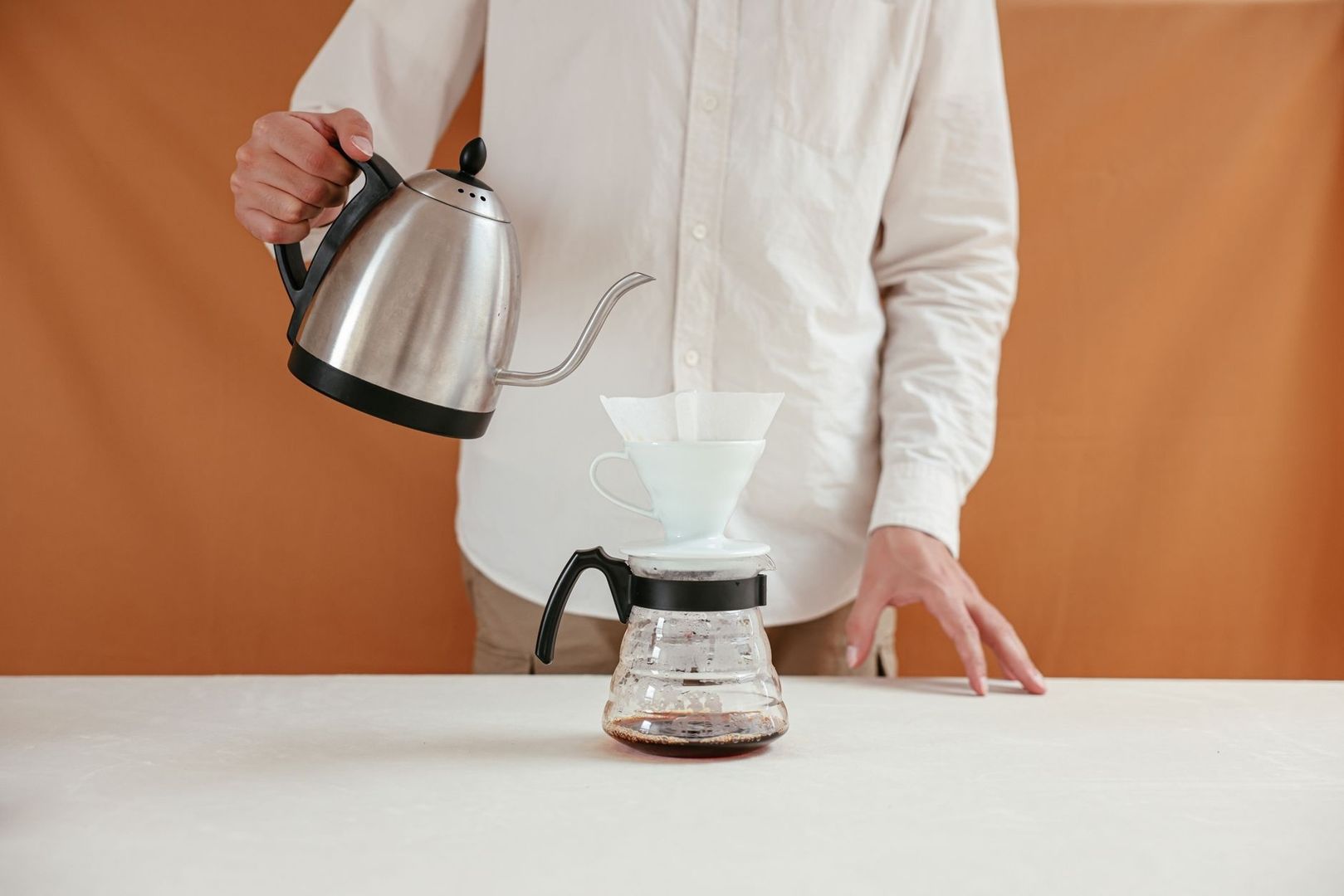 Person brüht Kaffee mit einem Schwanenhalskessel und Papierfilter auf