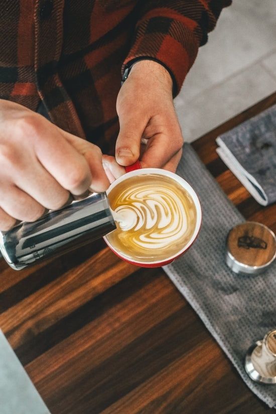 Barista gießt glänzenden Milchschaum mit einer Kanne in eine Tasse
